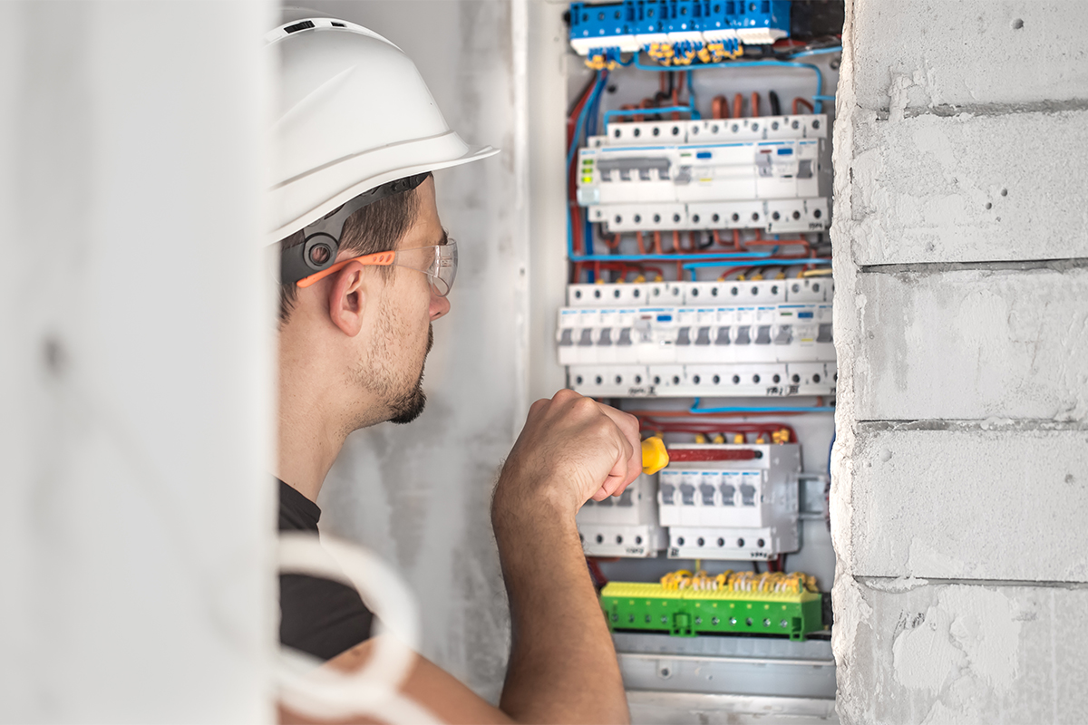 Man, an electrical technician working in a switchboard with fuses. Installation and connection of electrical equipment. Professional with tools in hand. concept of complex work, space for text.
